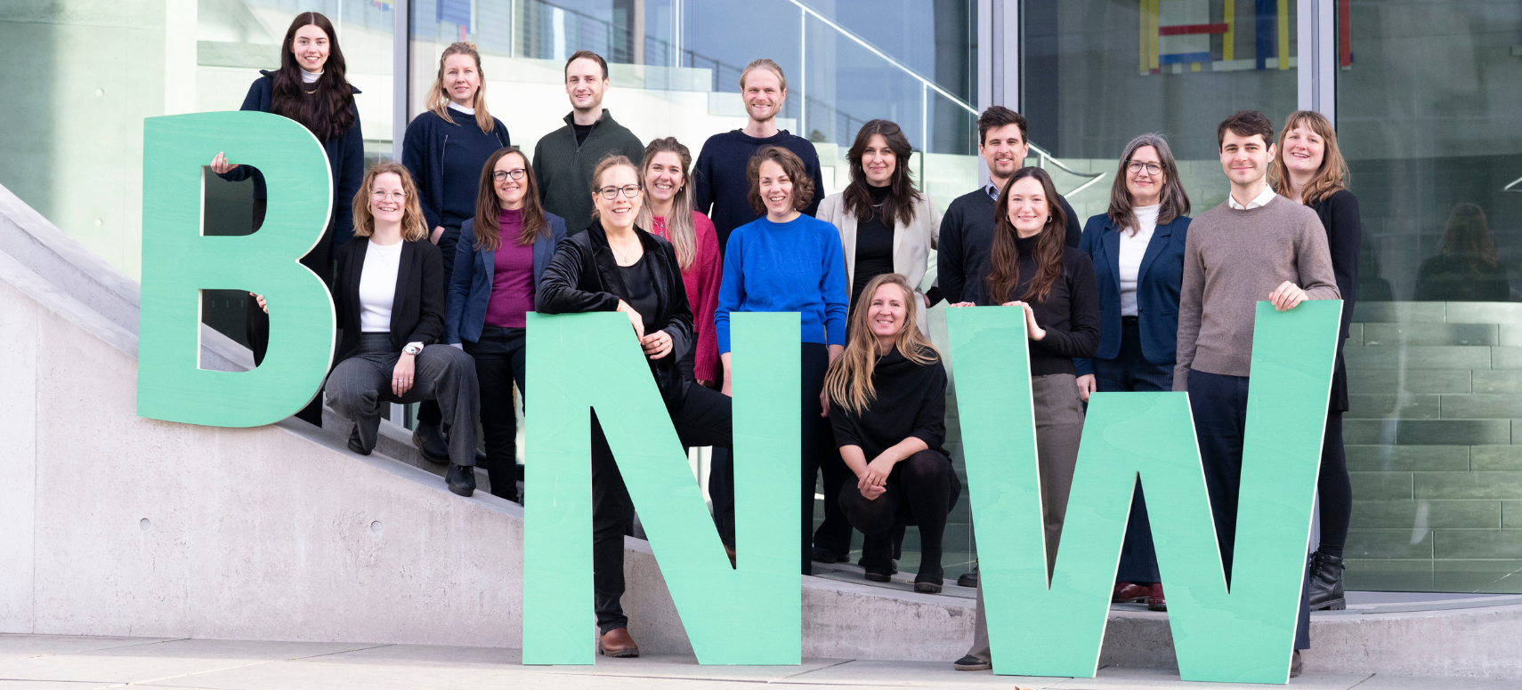 Das Team der BNW-Geschäftsstelle vor einem Fensterbogen des  Marie-Elisabeth-Lüders-Haus mit den Buchstaben BNW in grün